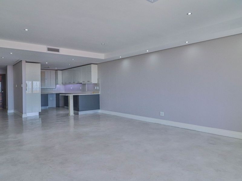 Spacious open-plan living area featuring polished concrete floors, recessed lighting, and a modern kitchen with built-in cabinetry and a breakfast peninsula.