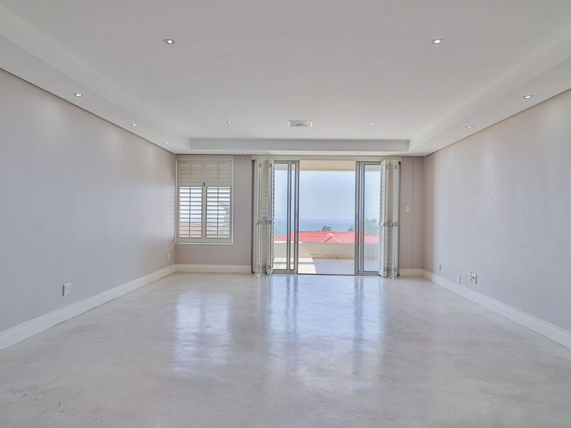 Spacious, light-filled living area featuring polished concrete floors, recessed ceiling lighting, and bi-fold doors opening to a balcony with scenic views.