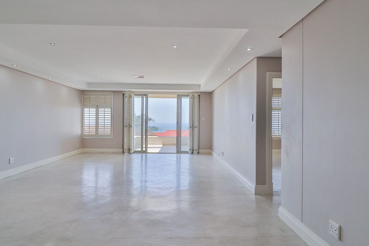 Spacious, light-filled living area featuring polished concrete floors, recessed ceiling lighting, and bi-fold doors opening to a balcony with ocean views.