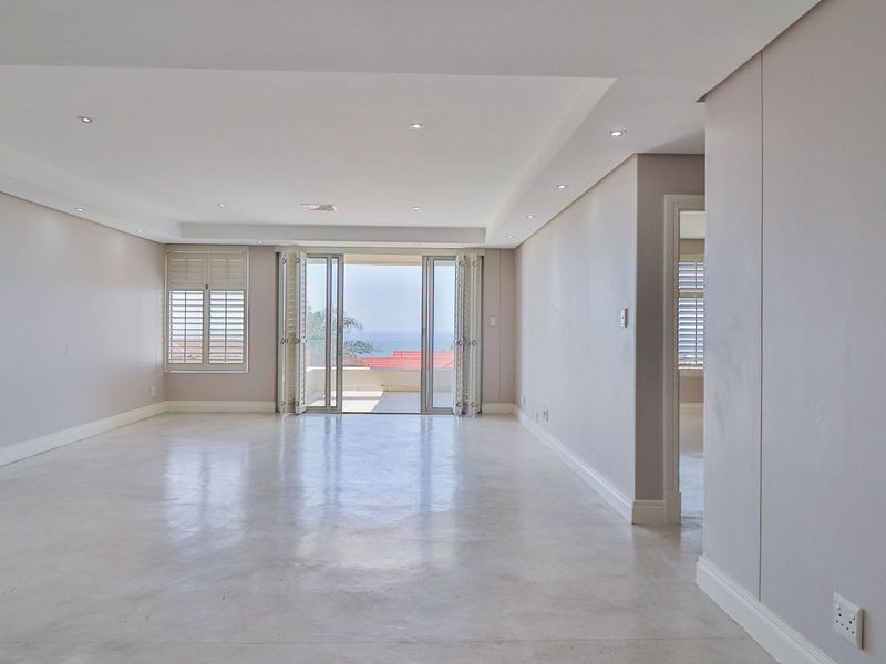 Spacious, light-filled living area featuring polished concrete floors, recessed ceiling lighting, and bi-fold doors opening to a balcony with ocean views.