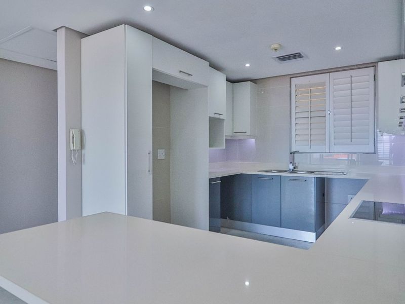 Modern kitchen featuring sleek white and grey cabinetry, stone countertops, integrated cooktop, extractor fan, and plantation shutters for natural light control.
