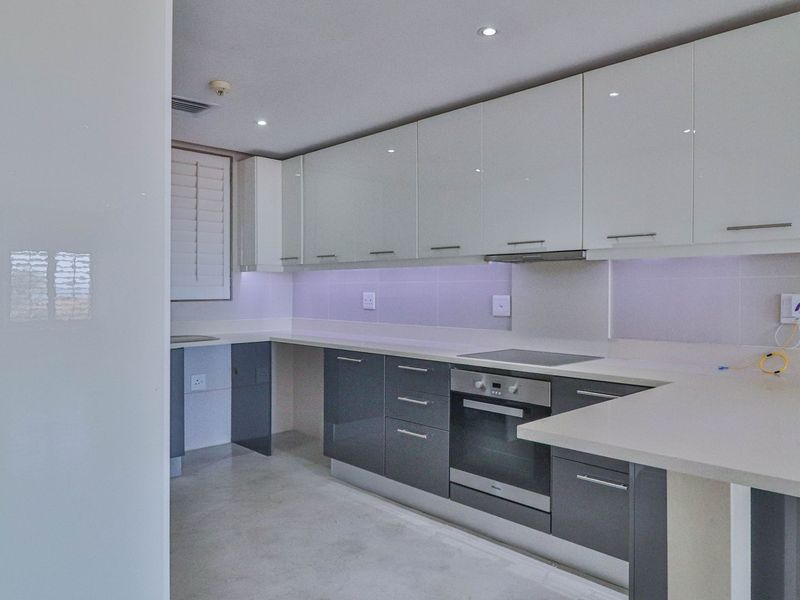 Modern kitchen featuring sleek high-gloss cabinetry, stone countertops, integrated oven, and hob, offering a clean and contemporary culinary space.