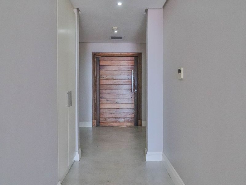A clean and modern entrance hallway featuring a solid timber front door, built-in storage cupboards, and neutral wall finishes.