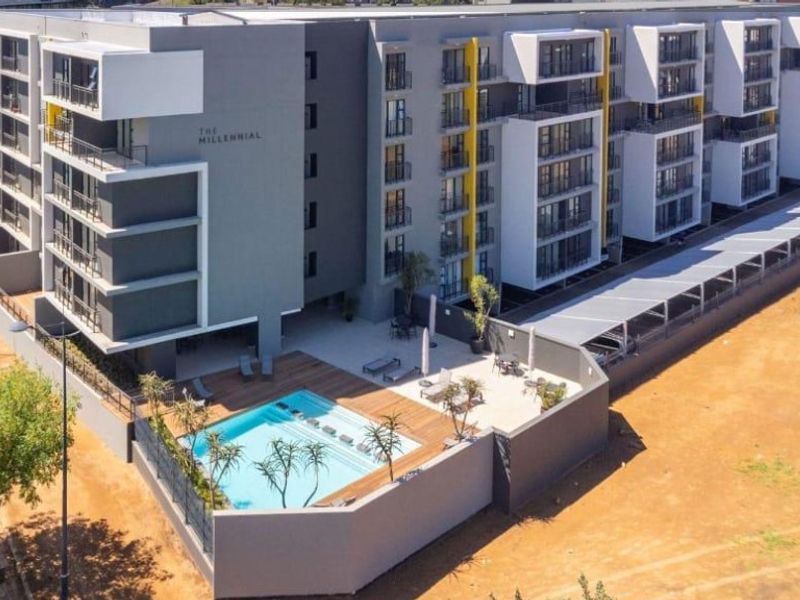 Aerial view of a modern apartment complex featuring a swimming pool, wooden decking, and covered parking facilities.
