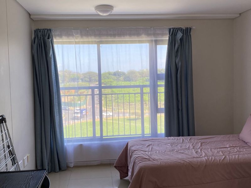A bright bedroom featuring large sliding glass doors with balcony access, tiled flooring, and neutral wall finishes.