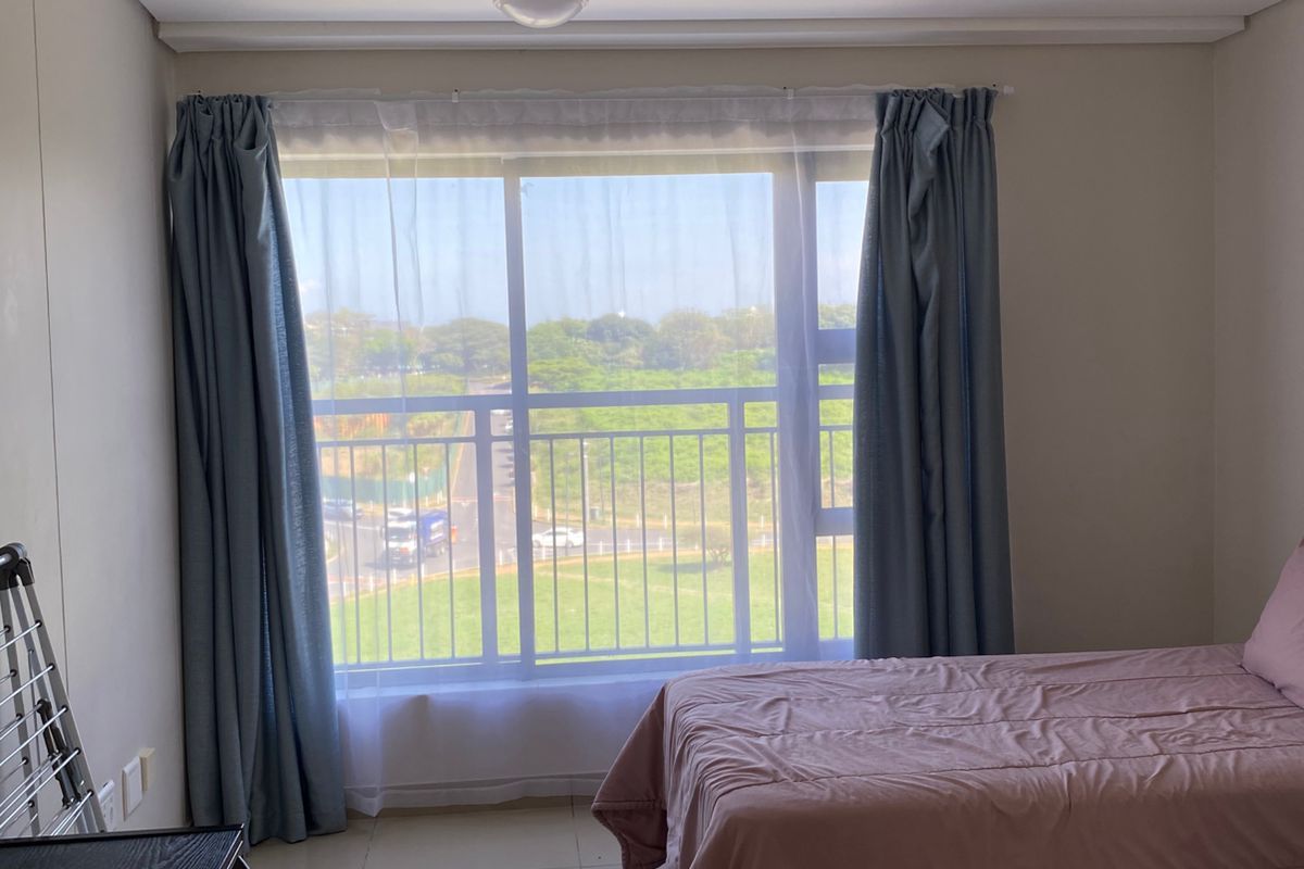 A bright bedroom featuring large sliding glass doors with balcony access, tiled flooring, and neutral wall finishes.