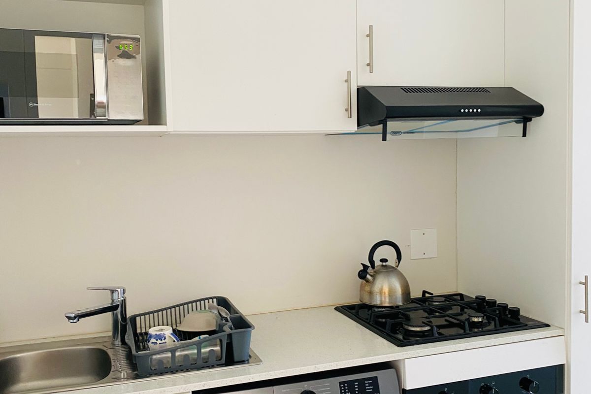 Compact modern kitchen featuring white cabinetry, stone countertops, integrated gas hob, oven, extractor fan, and space for a washing machine.