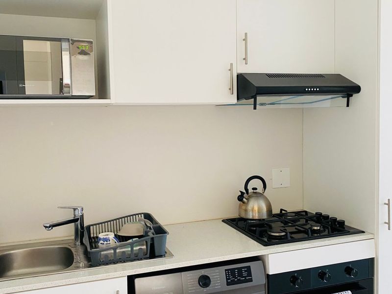 Compact modern kitchen featuring white cabinetry, stone countertops, integrated gas hob, oven, extractor fan, and space for a washing machine.