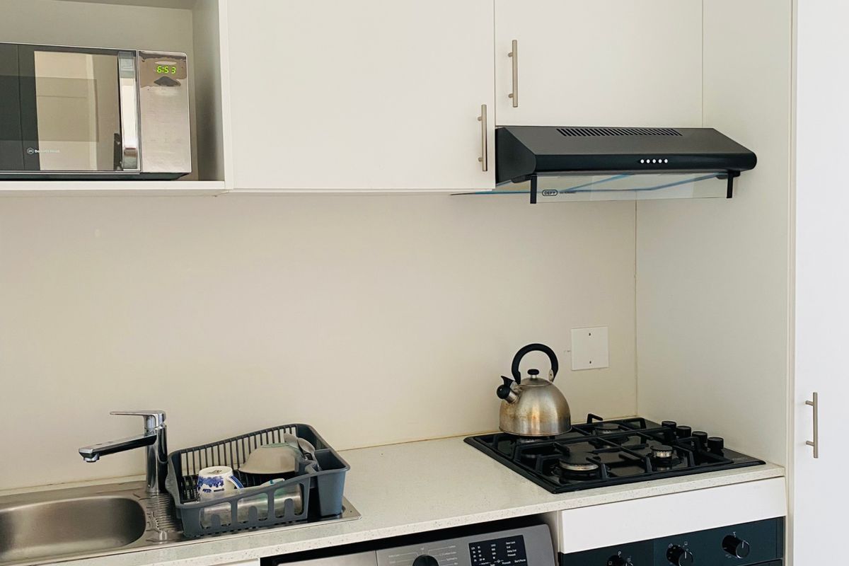 Compact modern kitchen featuring white cabinetry, gas hob, built-in oven, extractor fan, integrated washing machine, and a built-in microwave.