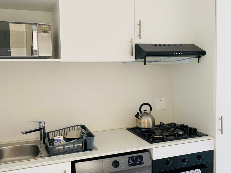 Compact modern kitchen featuring white cabinetry, gas hob, built-in oven, extractor fan, integrated washing machine, and a built-in microwave.
