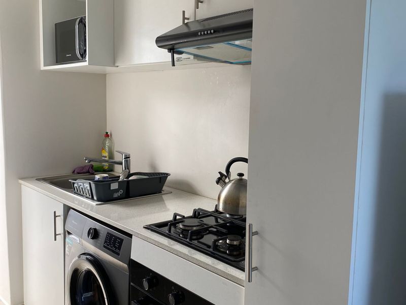 Compact modern kitchen featuring white cabinetry, stone countertops, integrated gas hob, oven, extractor fan, and space for a washing machine.