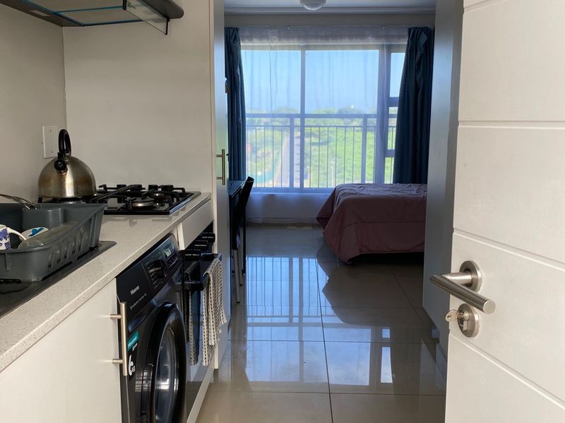 Compact open-plan apartment featuring a modern kitchen with gas hob and tiled flooring, leading into a bedroom area with large sliding glass doors.