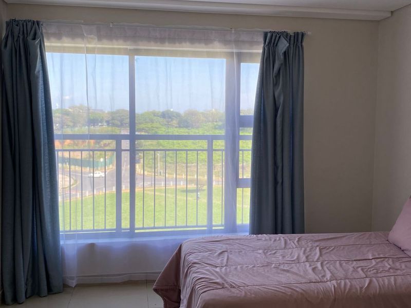 A bright bedroom featuring large windows with natural light, tiled flooring, and neutral wall finishes, offering a pleasant view of the surrounding area.