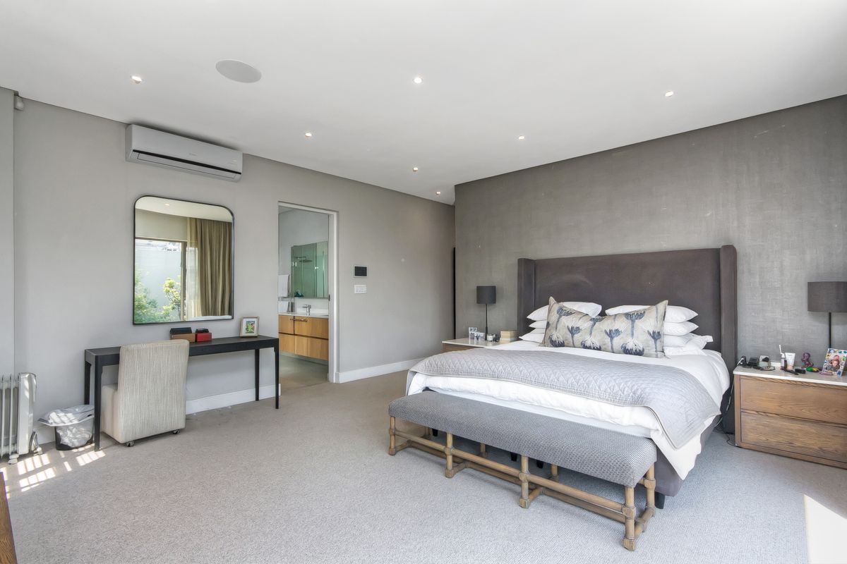 Spacious bedroom featuring neutral carpeting, recessed lighting, a wall-mounted air conditioning unit, and an en-suite bathroom.