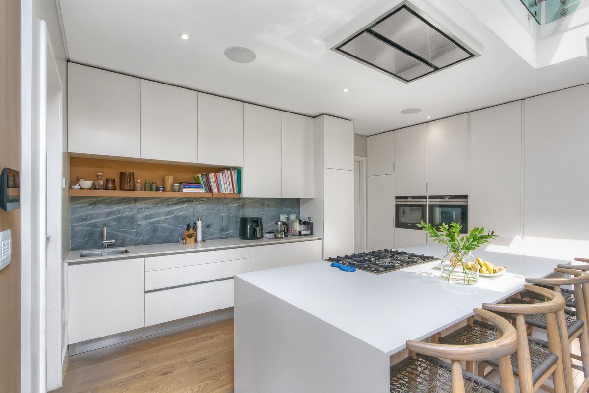 Modern kitchen featuring sleek white cabinetry, a central island with a gas hob, integrated double ovens, and a stone-tiled backsplash.