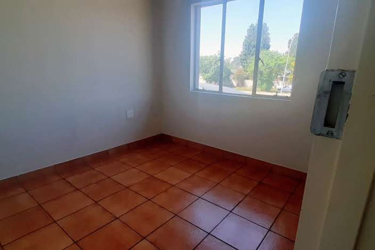A vacant bedroom featuring terracotta floor tiles and a large window, offering a blank canvas for personalization.