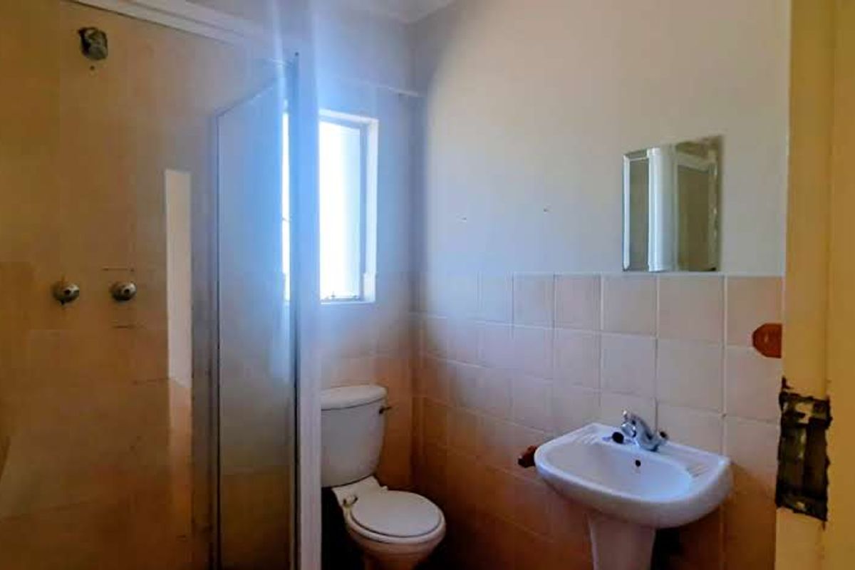 A compact bathroom featuring a glass-enclosed shower, pedestal basin, and toilet with neutral wall tiling.