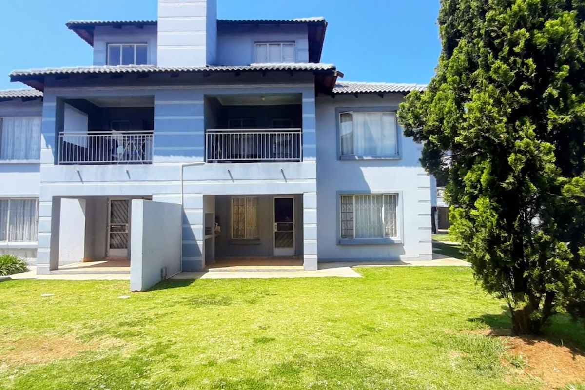 Rear view of a multi-story townhouse featuring a ground floor patio, upper-level balconies with metal railings, and a shared garden area.