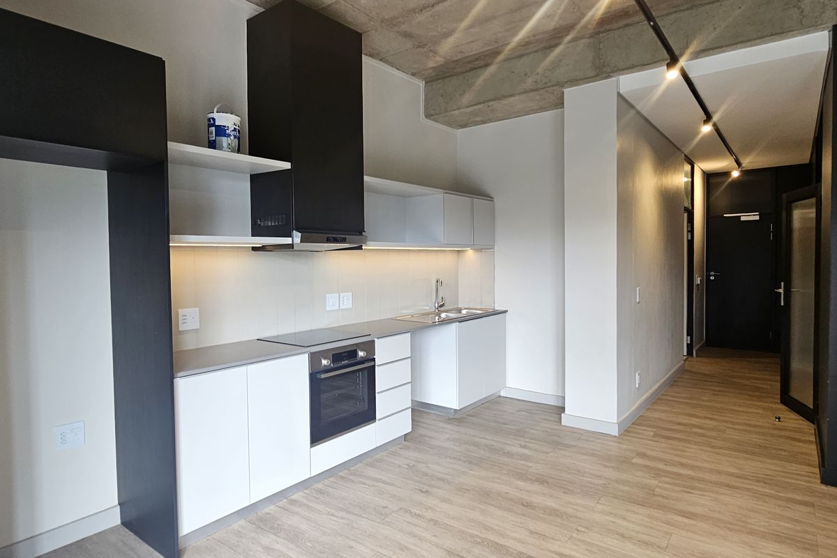 Modern open-plan kitchen featuring sleek white cabinetry, built-in oven, extractor fan, and exposed concrete ceiling detail.