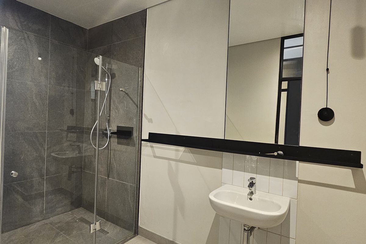 Modern bathroom featuring a glass-enclosed walk-in shower with dark grey tiling, a wall-mounted basin, and a large vanity mirror.