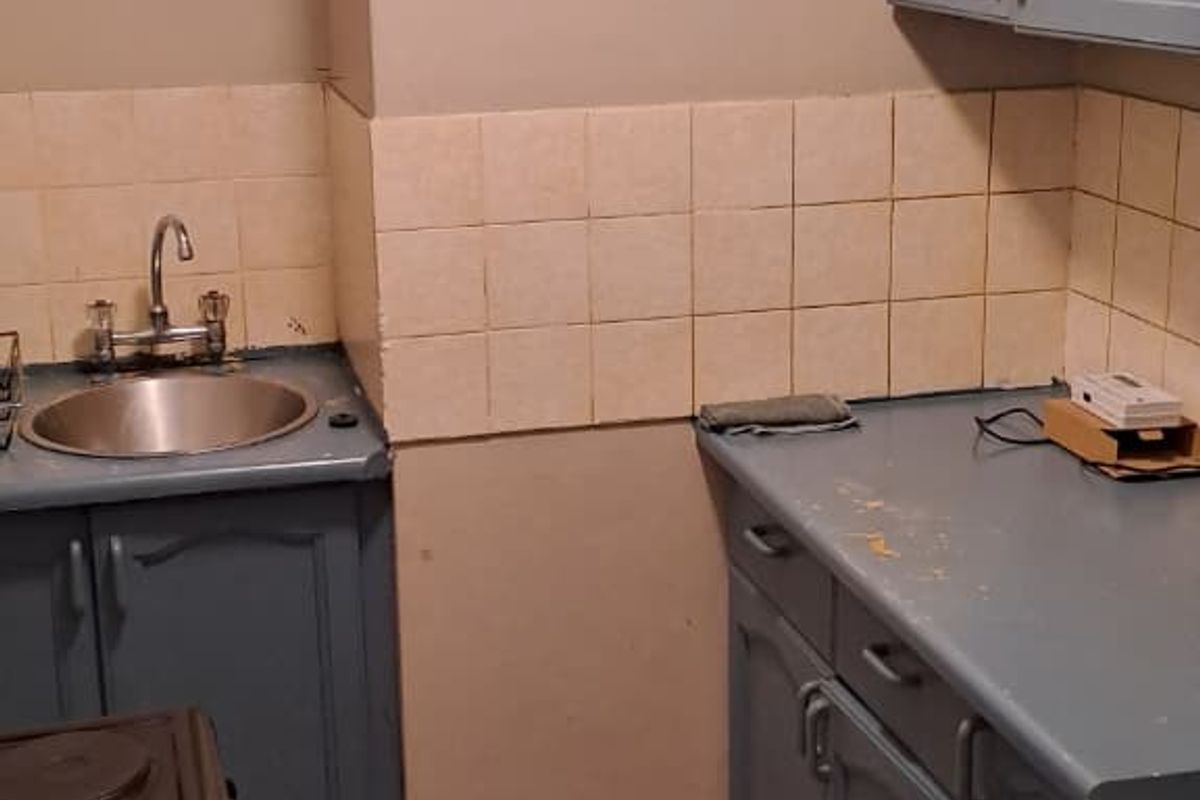 A compact kitchen featuring blue cabinetry, tiled backsplash, and tiled flooring, requiring cosmetic updates to improve its overall condition and appeal.