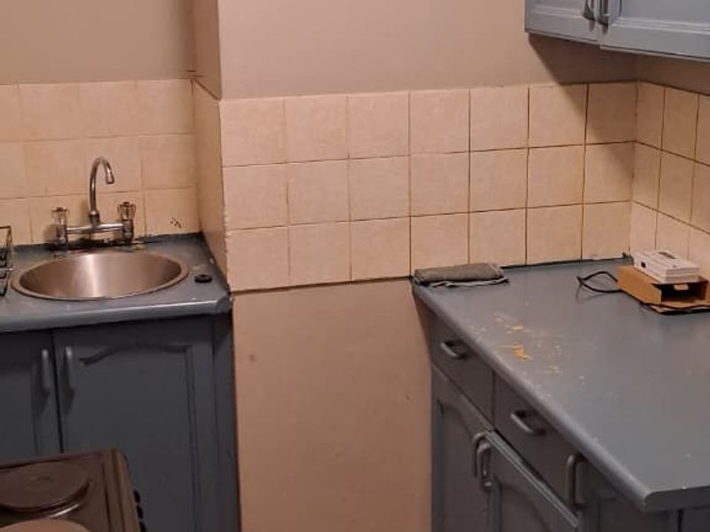 A compact kitchen featuring blue cabinetry, tiled backsplash, and tiled flooring, requiring cosmetic updates to improve its overall condition and appeal.