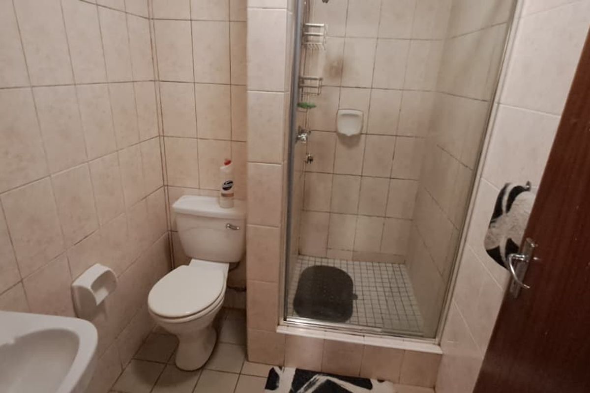 A compact bathroom featuring a shower enclosure, toilet, and washbasin with tiled walls and flooring, requiring cosmetic updates to improve its overall condition.
