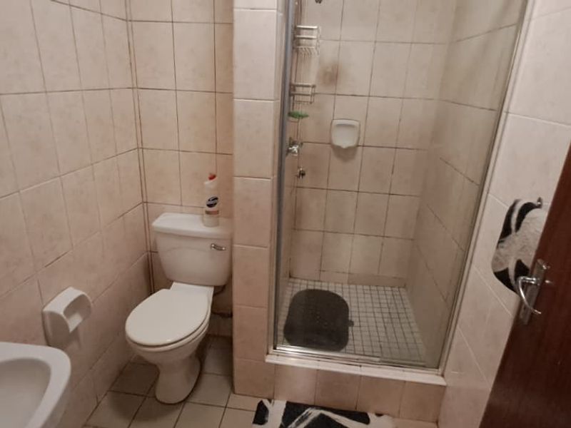A compact bathroom featuring a shower enclosure, toilet, and washbasin with tiled walls and flooring, requiring cosmetic updates to improve its overall condition.