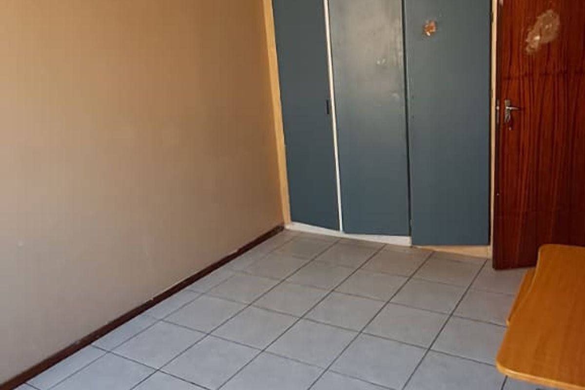 An empty bedroom featuring tiled flooring, a ceiling light fixture, and built-in cupboards with a wooden door entrance.