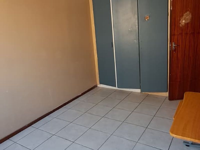 An empty bedroom featuring tiled flooring, a ceiling light fixture, and built-in cupboards with a wooden door entrance.