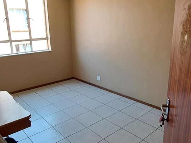 An empty bedroom featuring tiled flooring, a large window, and a ceiling light fixture, ready for renovation or staging.