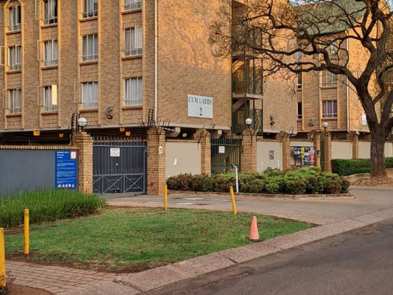 Street view of the apartment complex entrance featuring face brick architecture, secure gated access, and perimeter walling with electric fencing.