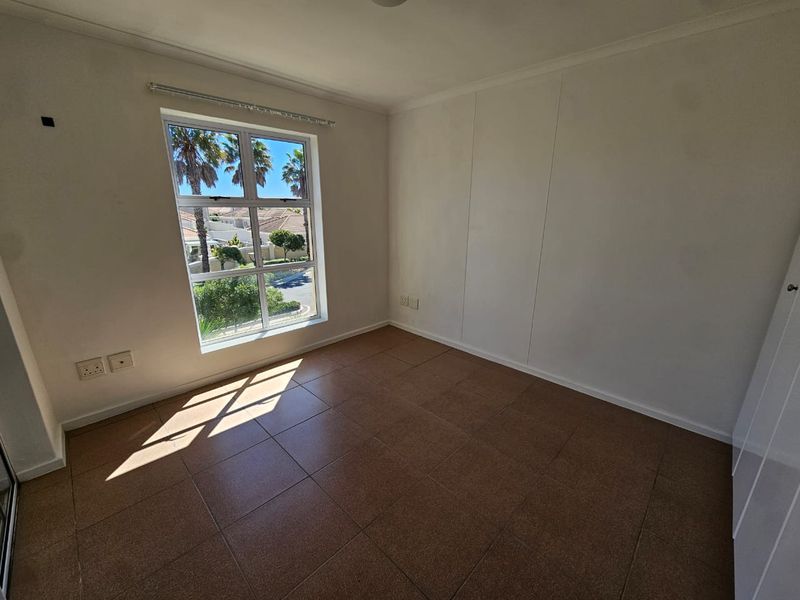 A vacant bedroom featuring tiled flooring, built-in cupboards, and a window providing natural light and exterior views.