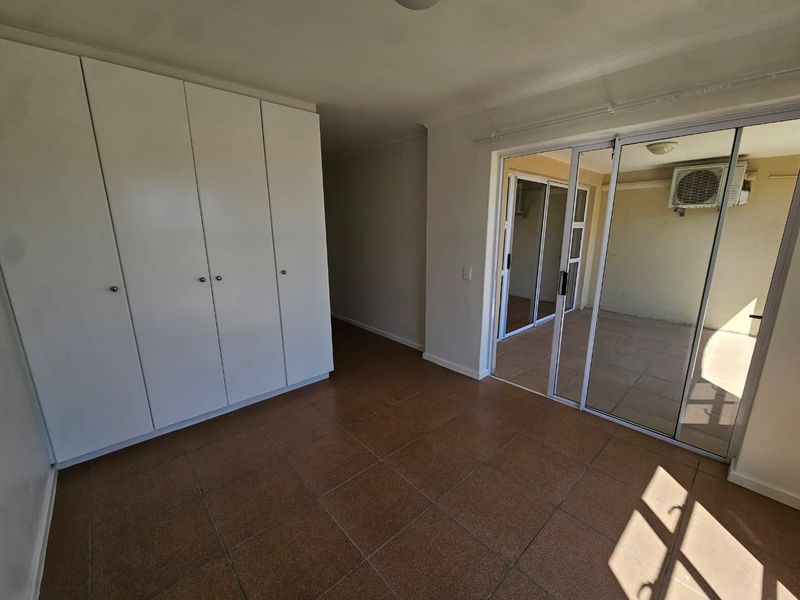 An empty bedroom featuring built-in cupboards, tiled flooring, and sliding glass doors leading to an outdoor balcony area.