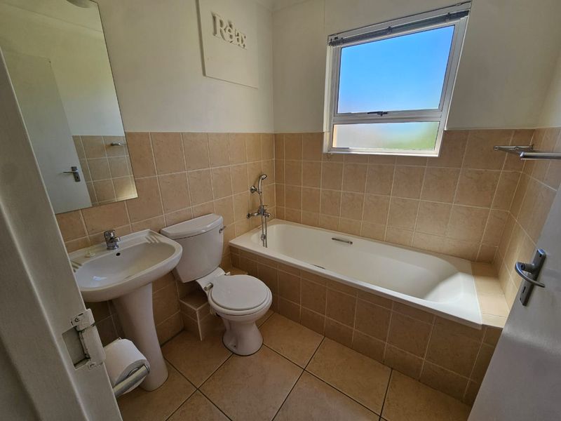 A functional bathroom featuring a pedestal basin, toilet, and a tiled built-in bathtub with neutral wall and floor tiling.
