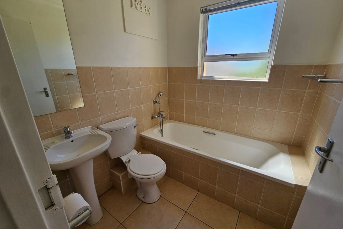 A functional bathroom featuring a pedestal basin, toilet, and a tiled built-in bathtub with neutral wall and floor tiling.