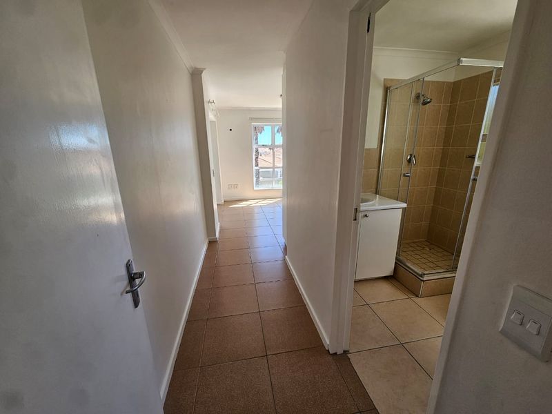 A hallway leading to a living area, featuring tiled flooring and access to a bathroom with a shower enclosure and vanity basin.