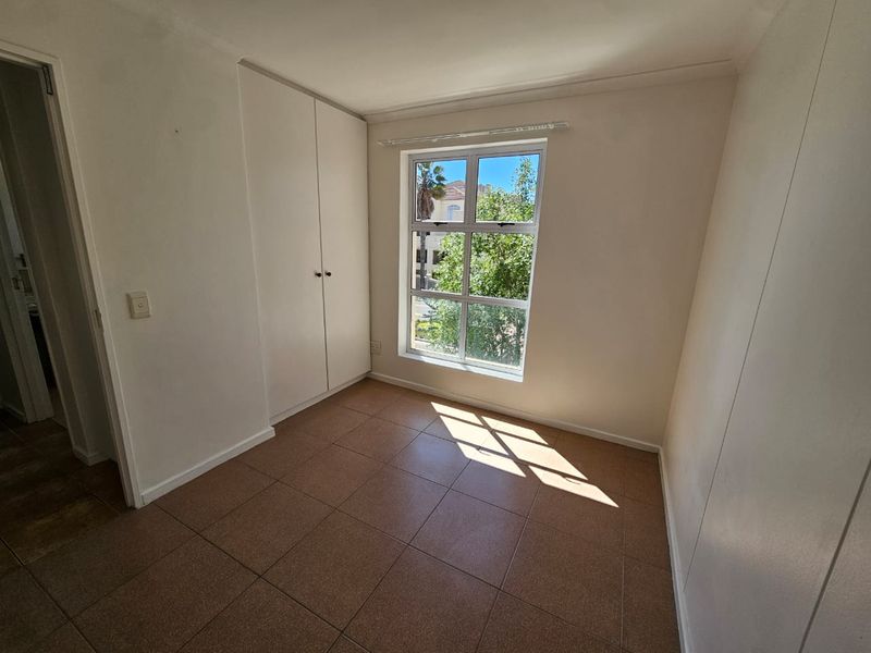 A bright, empty bedroom featuring tiled flooring and built-in cupboards, offering a clean and neutral space ready for personalization.