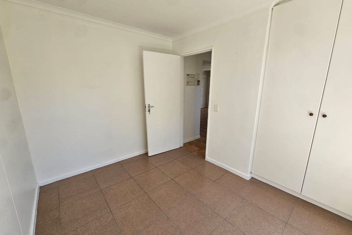 A clean, empty bedroom featuring neutral tiled flooring and built-in cupboards, offering a blank canvas for personalization.