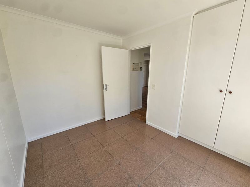 A clean, empty bedroom featuring neutral tiled flooring and built-in cupboards, offering a blank canvas for personalization.