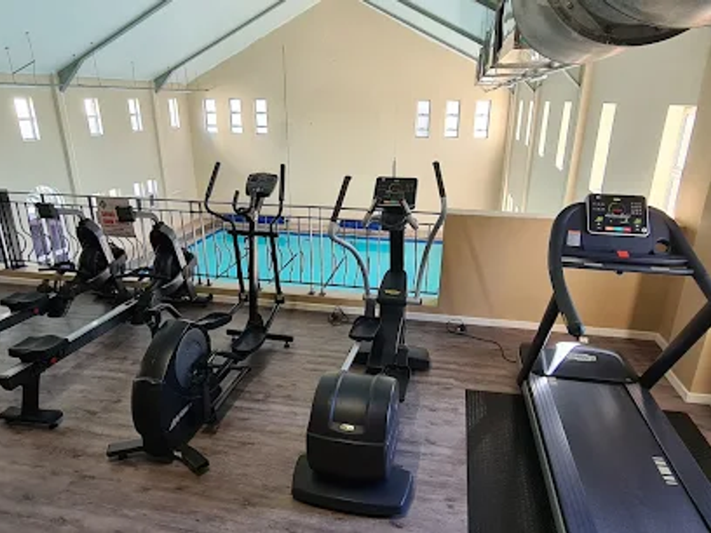 Spacious gym area featuring vaulted ceilings, exposed ductwork, and a mezzanine view overlooking the indoor pool area.