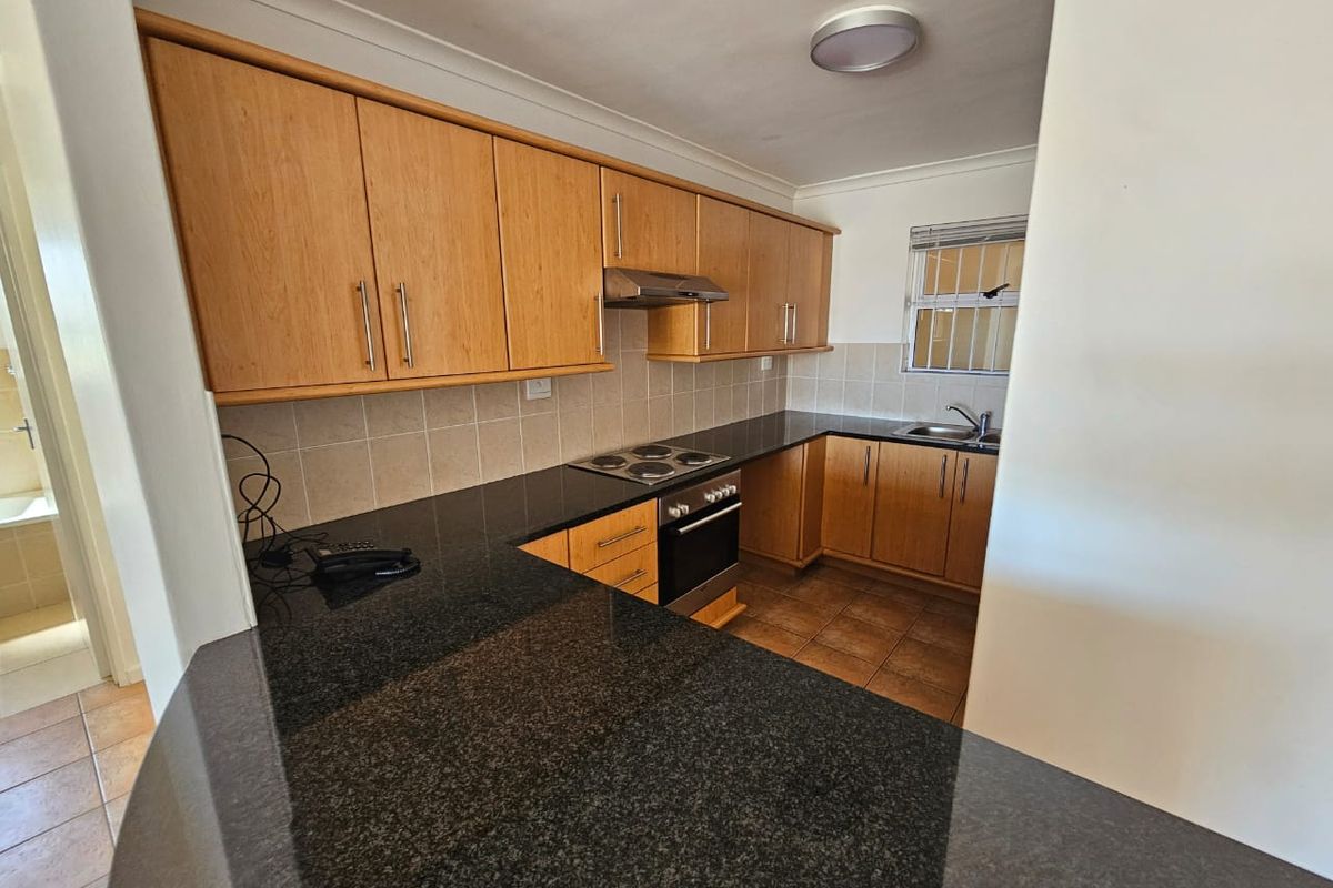 A functional kitchen featuring granite countertops, wooden cabinetry, built-in oven, electric hob, and tiled finishes, offering a clean and practical workspace.