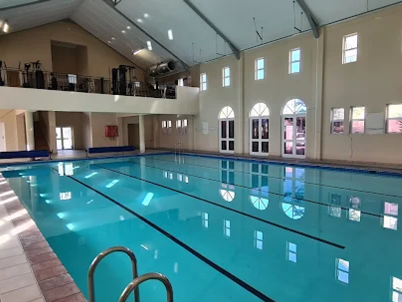 Spacious indoor swimming pool area featuring a mezzanine level, arched windows, and tiled surrounds, providing a well-maintained communal leisure facility.