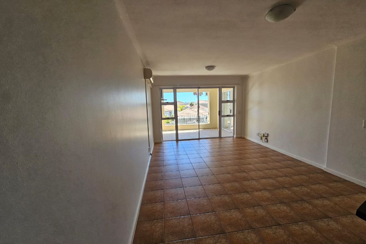 Spacious, empty living area featuring tiled flooring, an air conditioning unit, and large sliding glass doors leading to an outdoor balcony.