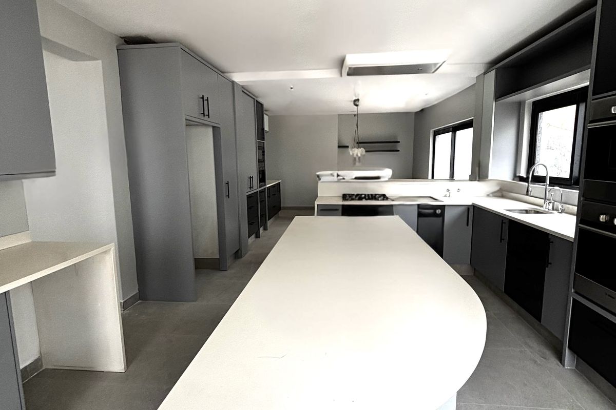 Modern kitchen featuring a large central island with a curved countertop, sleek grey cabinetry, integrated appliances, and tiled flooring.