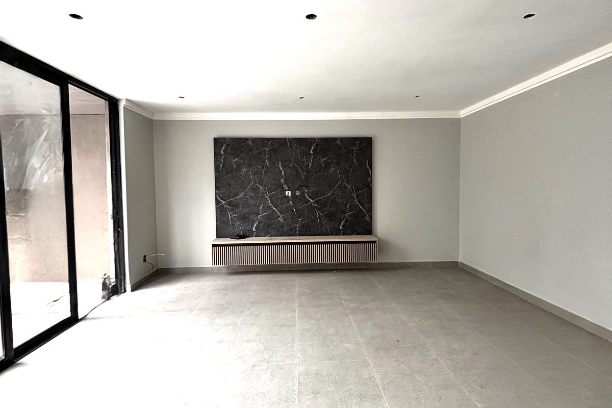 A spacious, modern living area featuring large format floor tiles, recessed ceiling lighting, and a contemporary built-in media console with a marble-effect feature wall.