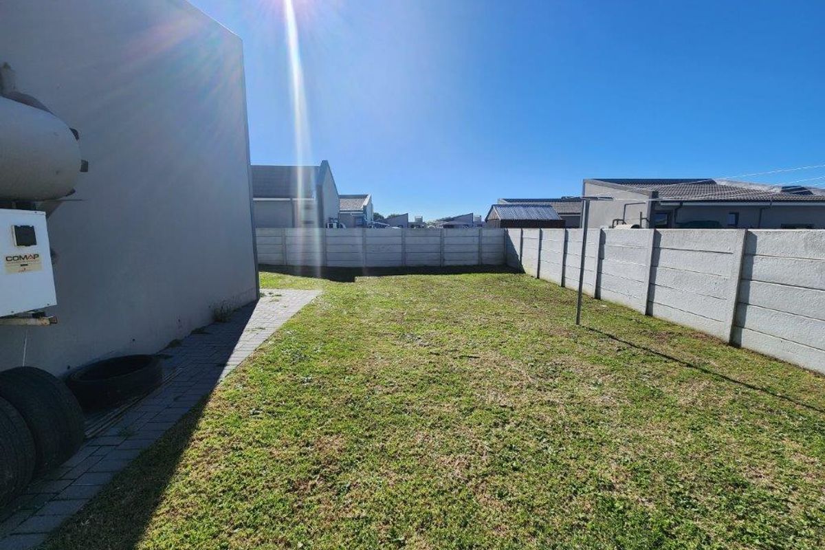 A private rear garden area featuring a grass lawn, paved walkway, and perimeter boundary walls, providing a functional outdoor space for the townhouse.