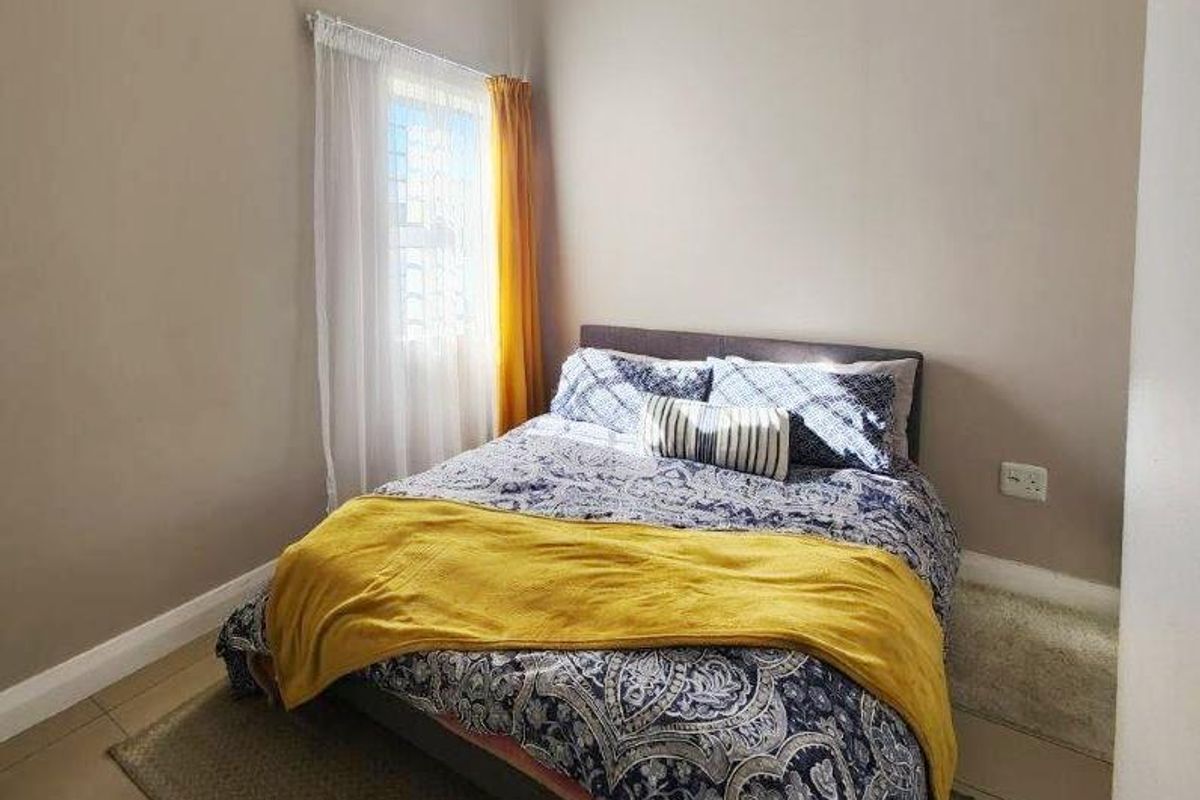 A compact bedroom featuring neutral wall tones, tiled flooring, and a window with curtain fixtures.