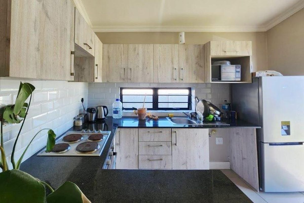 Modern kitchen featuring light wood-grain cabinetry, dark granite countertops, a built-in electric hob, and white subway tile backsplash.