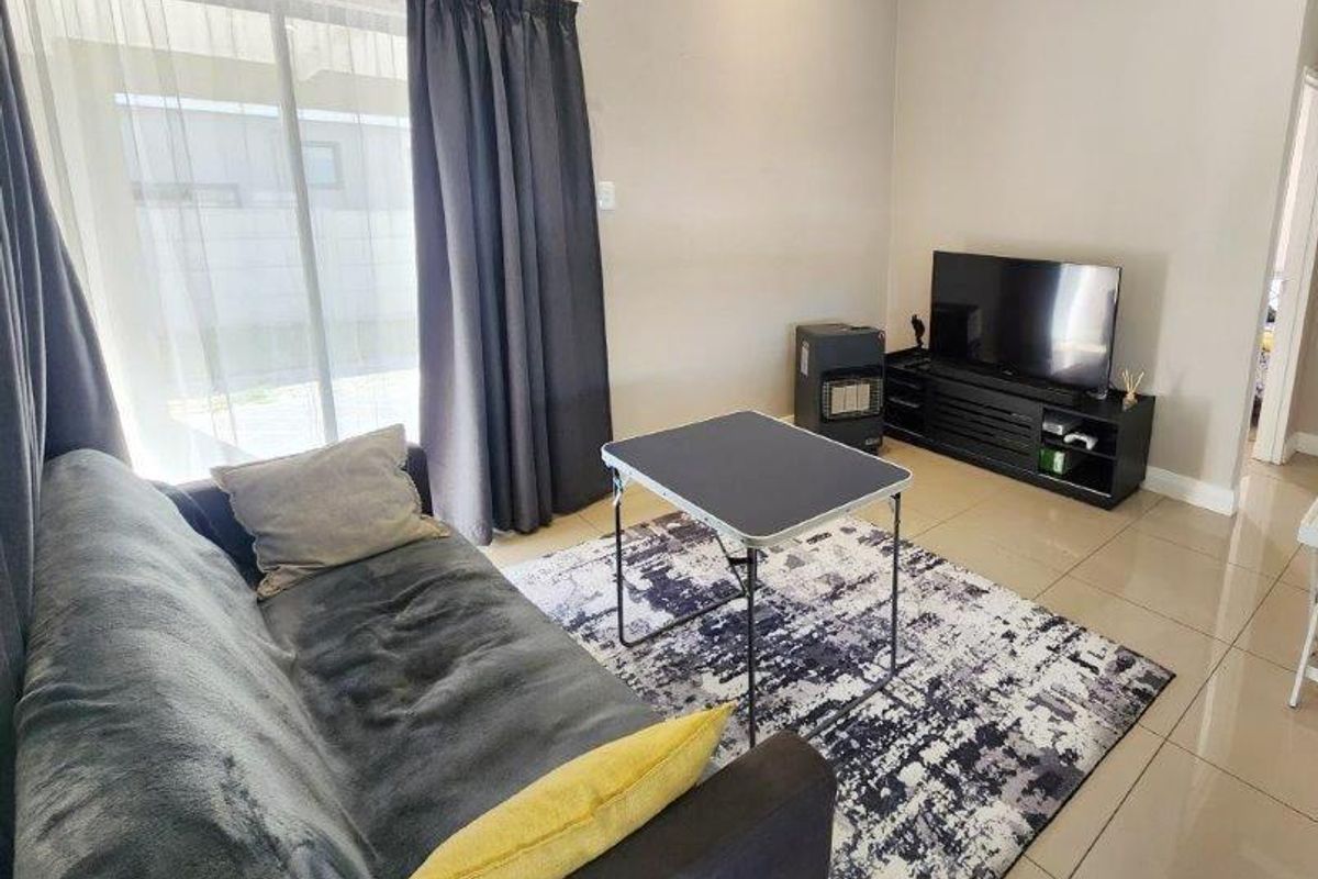 A living room featuring large sliding glass doors with curtains, tiled flooring, and a neutral wall finish.